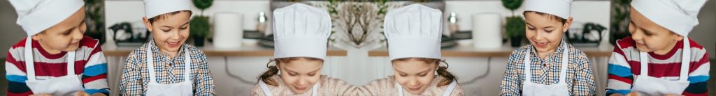 Children in chef hats cooking together in a classroom kitchen.